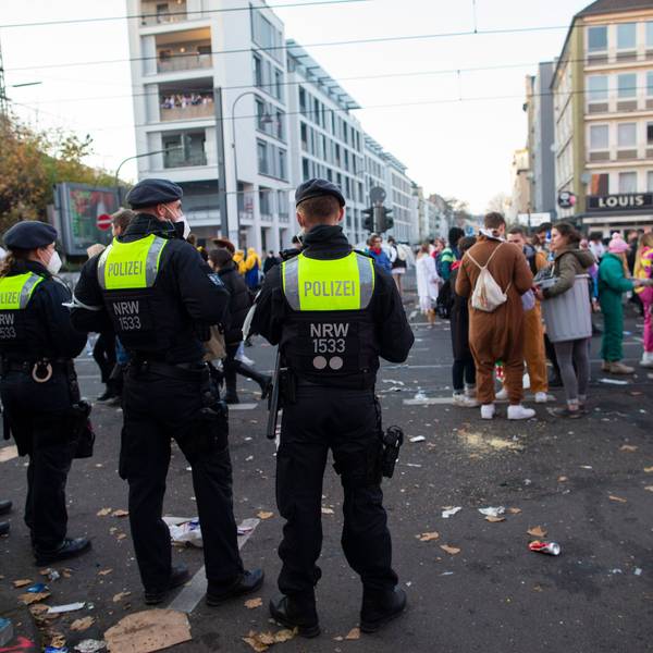 Junge Menschen feiern an der Zülpicher Strasse Karneval. Davor stehen Polizeibeamte und beobachten das Geschehen.