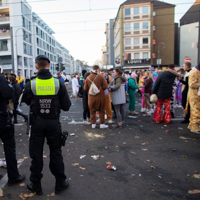 Junge Menschen feiern an der Zülpicher Strasse Karneval. Davor stehen Polizeibeamte und beobachten das Geschehen.