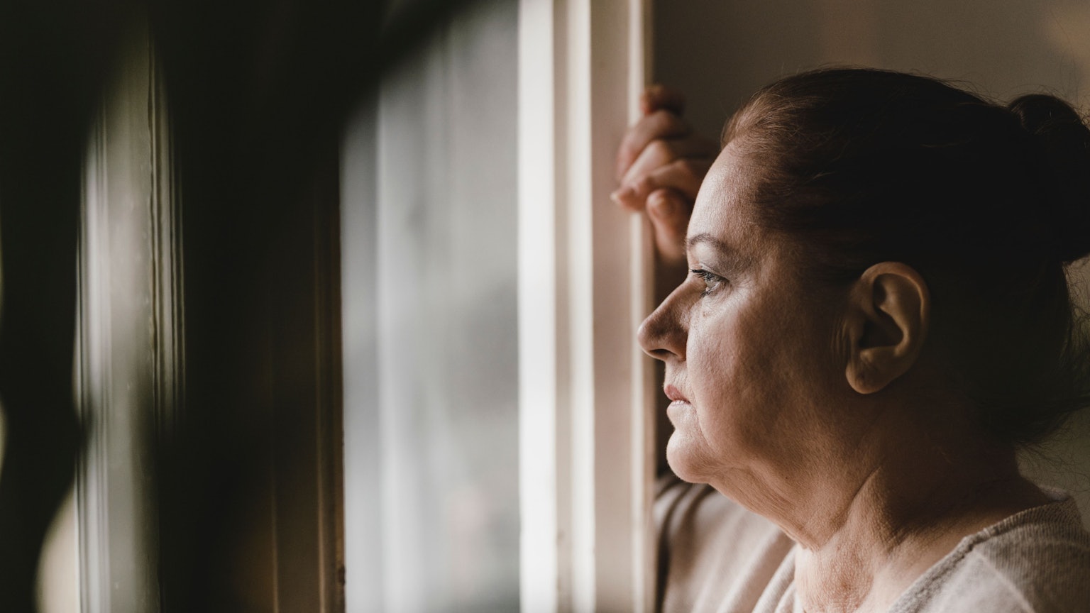 Deprimierte ältere Frau blickt sorgenvoll aus dem Fenster.
