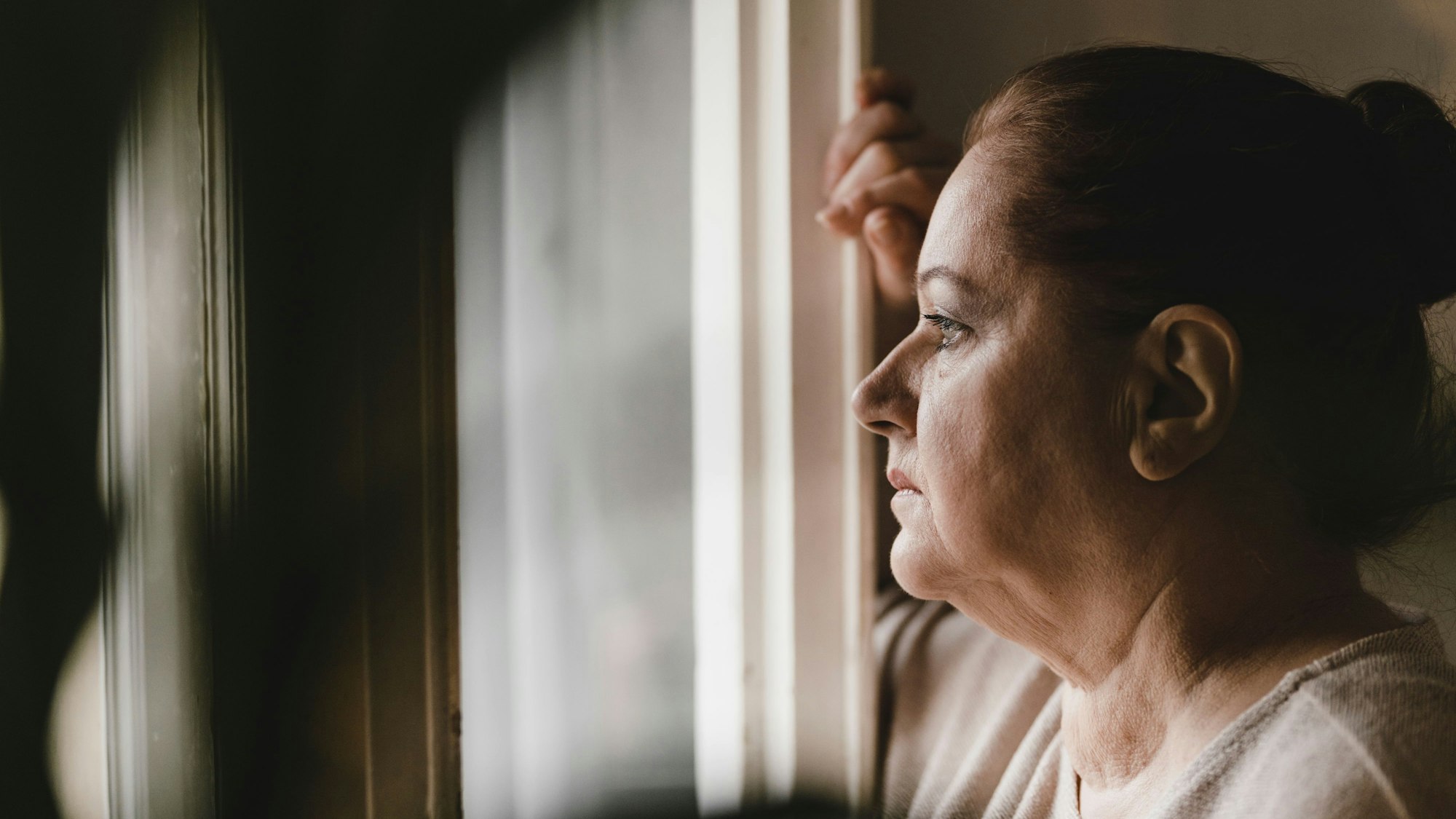 Deprimierte ältere Frau blickt sorgenvoll aus dem Fenster.