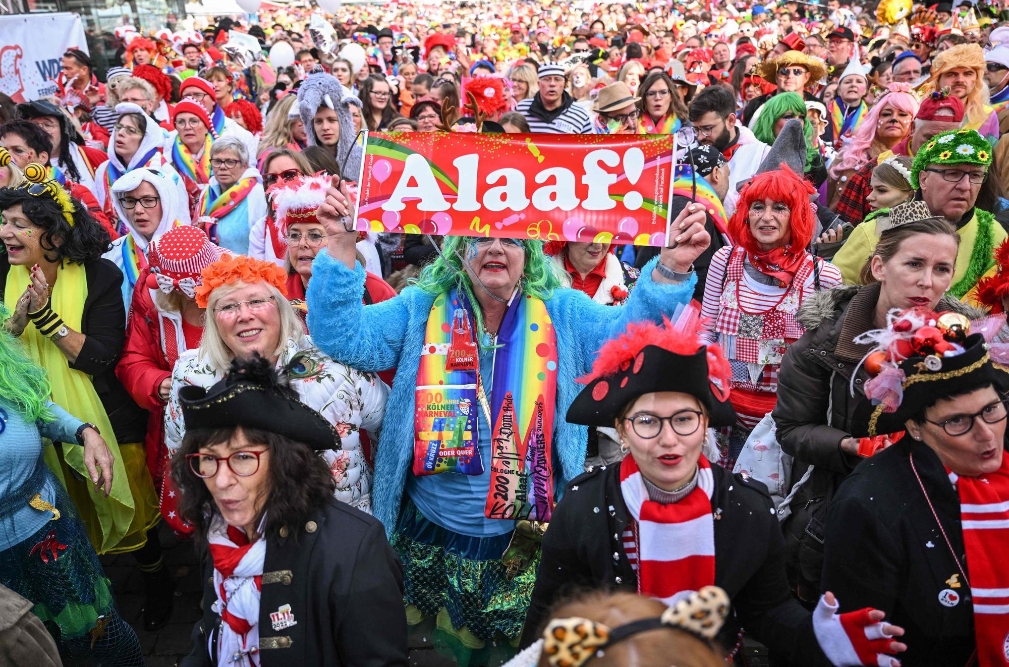 Feiernde am Heumarkt Köln. Eine verkleidete Frau hält ein Schild mit der Aufschrift „Alaaf!“ in die Luft.
