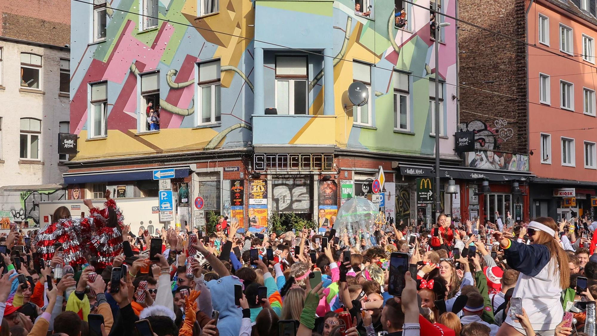 Die Zülpicher Straße, mit Blickrichtung auf die Kneipe "Der Stiefel" am 11.11. zum Karnevals-Sessionsauftakt. An der Kreuzung hat sich eine große Menge junger, verkleideter Menschen angesammelt.