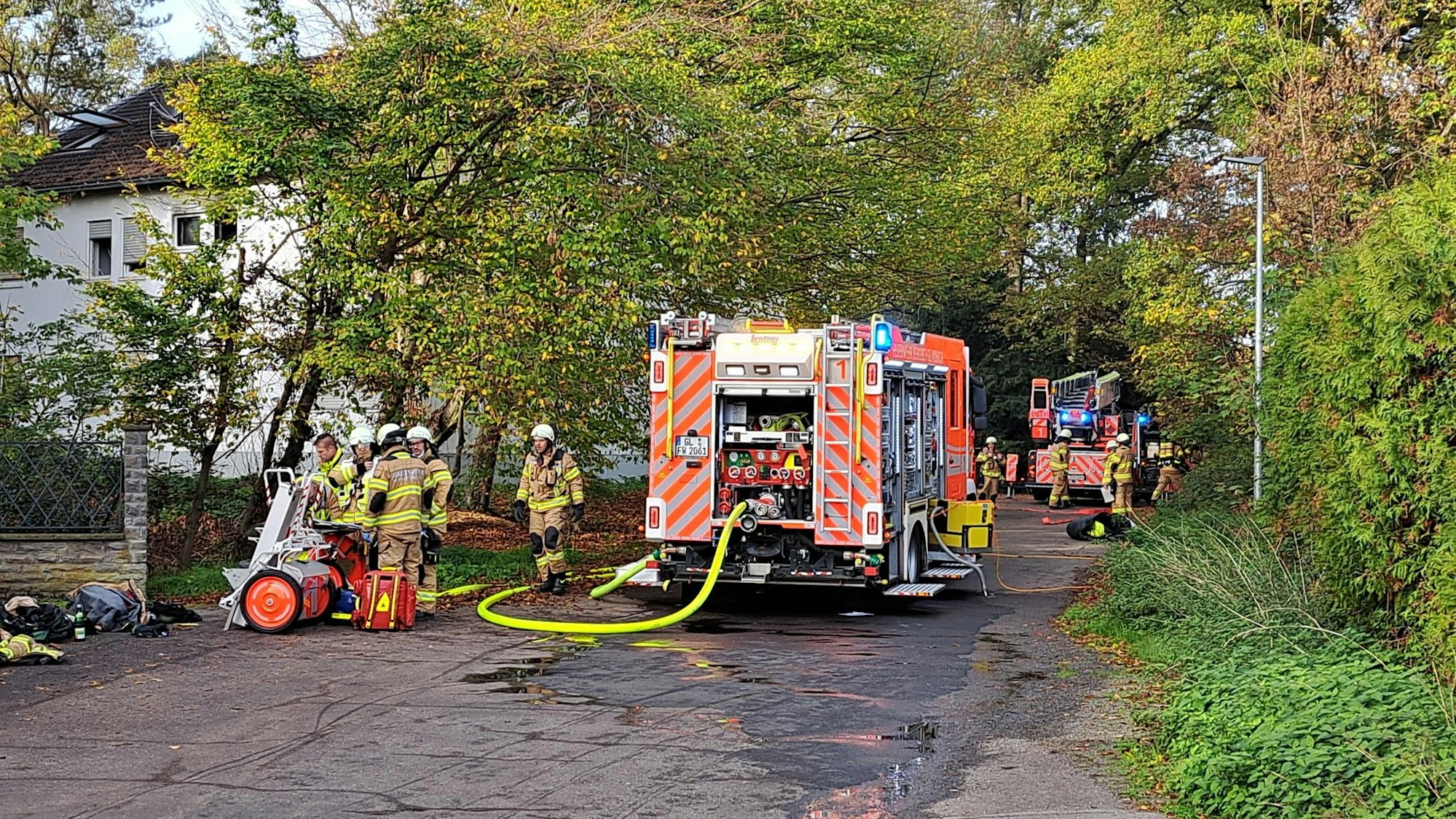 Zwei große Einsatzwagen und mehrere Feuerwehrleute stehen vor dem ausgebrannten Haus.