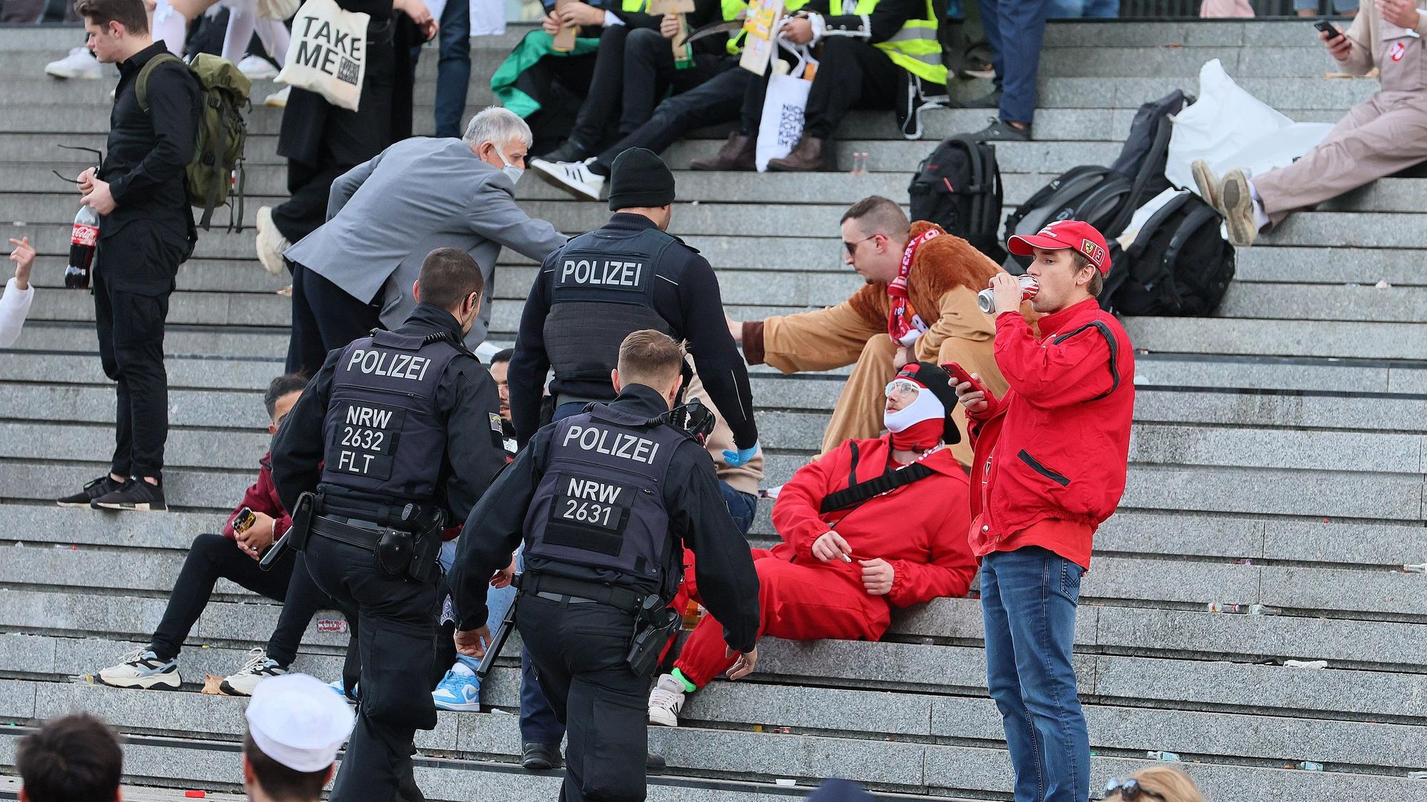 Drei Beamte der Polizei gehen auf die Personen auf der Domtreppe zu.