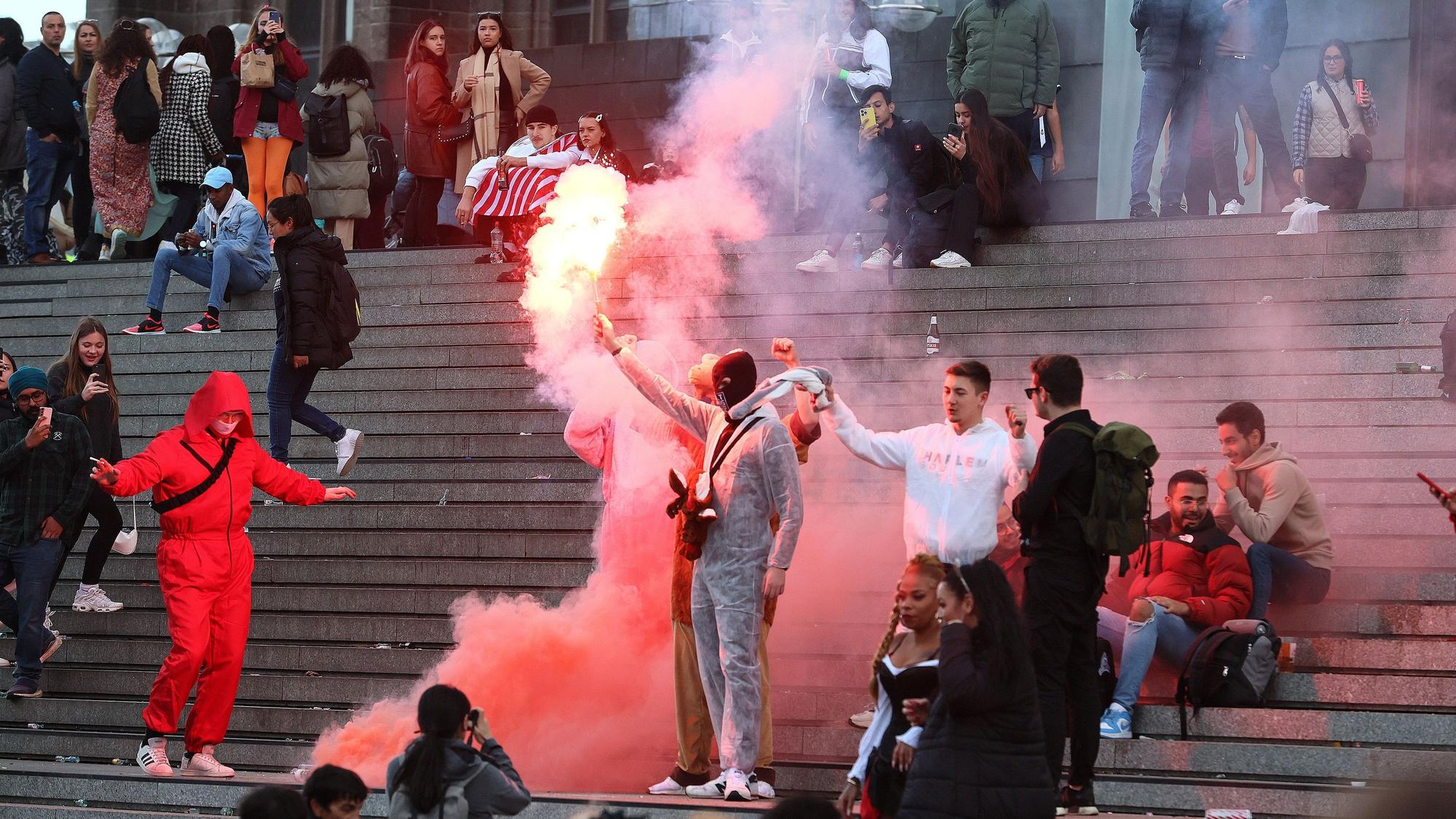 Mehrere Personen sitzen auf der Domtreppe. Ein Mann mit Ganzkörperanzug hat ein leuchtendes Bengalo in der Hand.