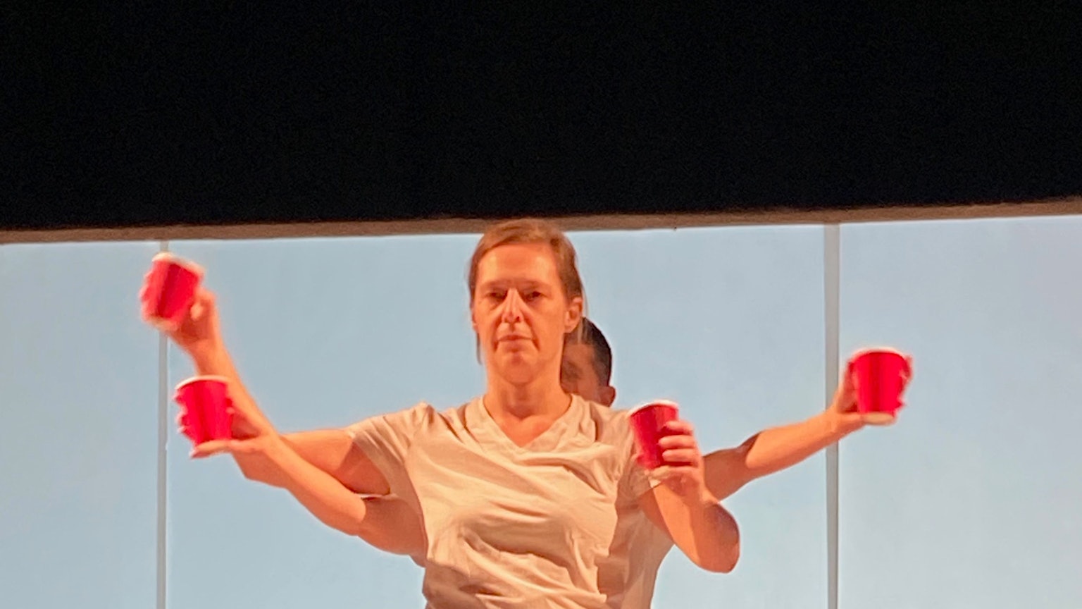 Zwei Mitglieder der "performing group" greifen in ihrer Darstellung auf der Bühne mit roten Einwegbechern das Thema Konsum kritisch auf.