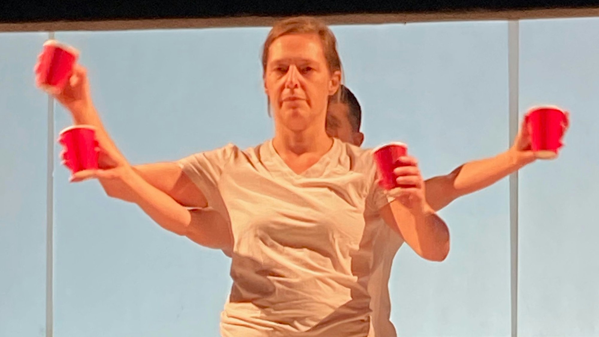 Zwei Mitglieder der "performing group" greifen in ihrer Darstellung auf der Bühne mit roten Einwegbechern das Thema Konsum kritisch auf.