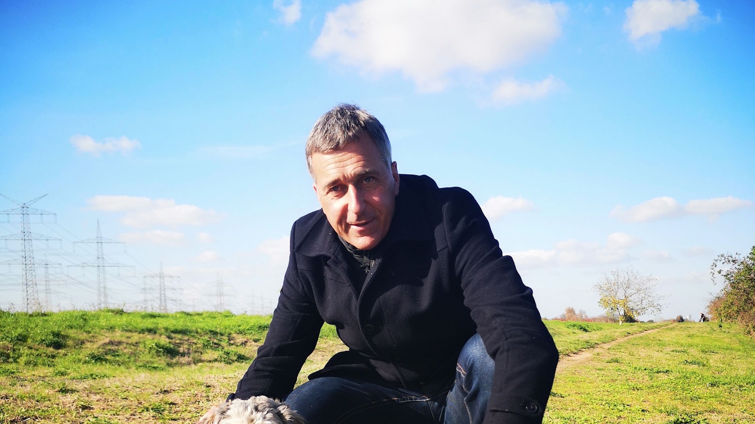 Bürgermeisterkandidat Ralph Manzke hockt mit zwei kleinen, weißen Hunden auf einer Wiese.