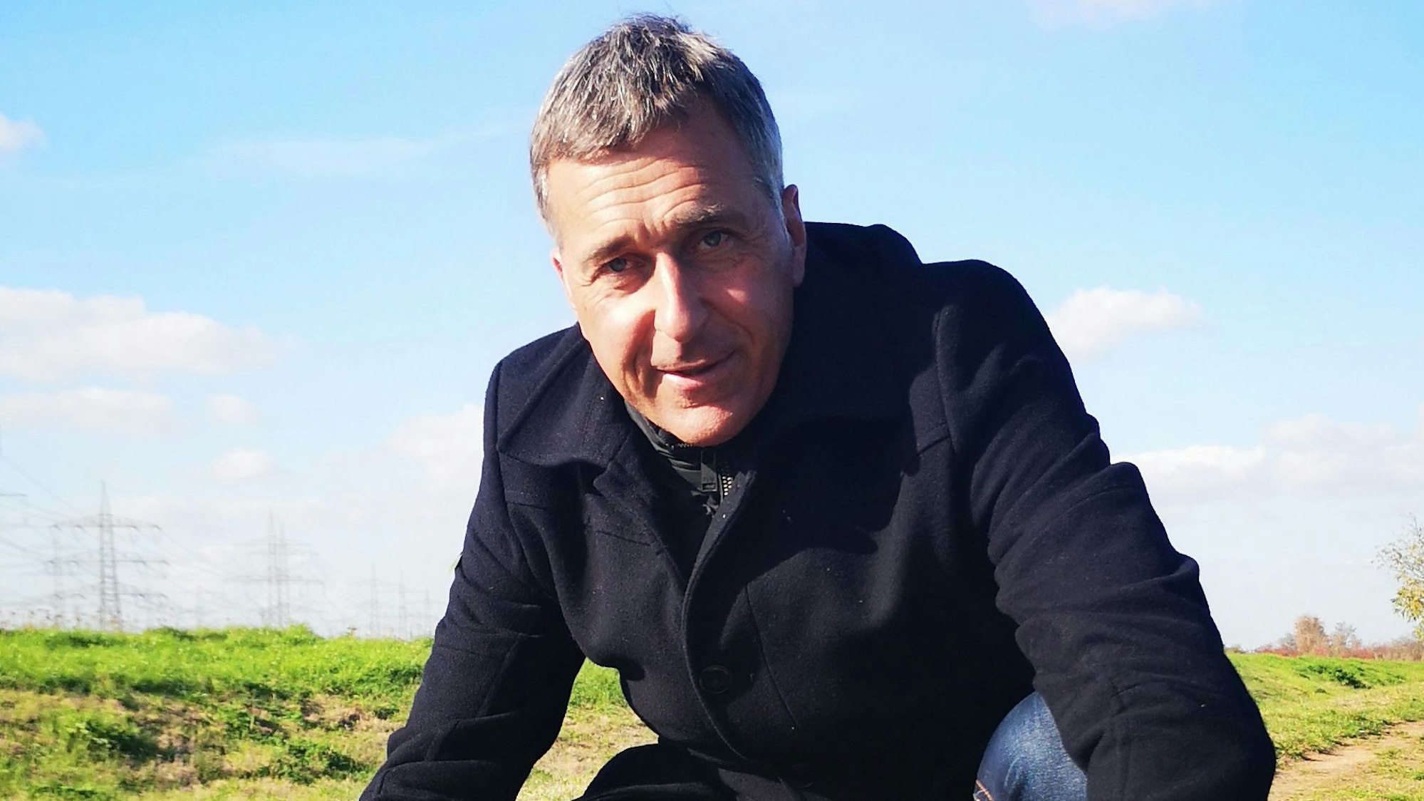 Bürgermeisterkandidat Ralph Manzke hockt mit zwei kleinen, weißen Hunden auf einer Wiese.