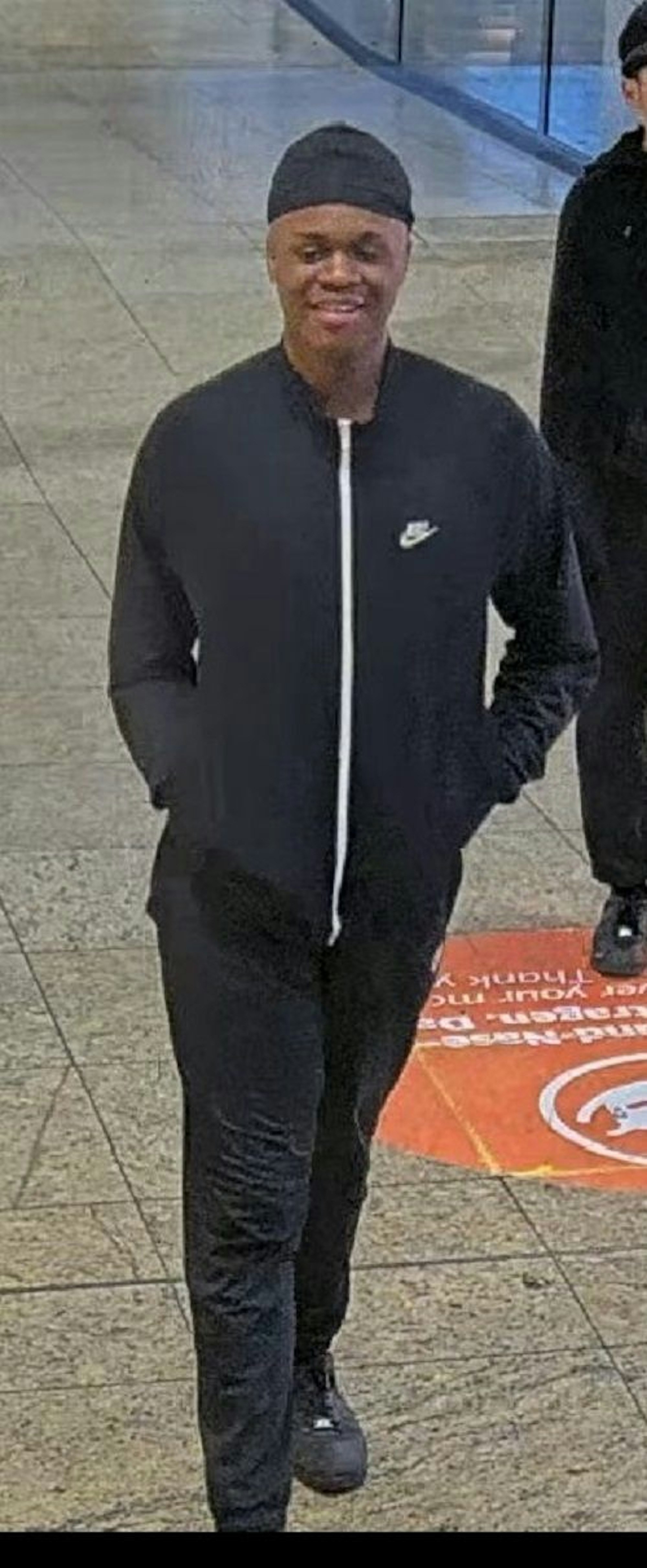 Der zweite Verdächtigte trägt eine schwarze Trainingshose, Sportschuhe und eine schwarze, eng anliegende Mütze.