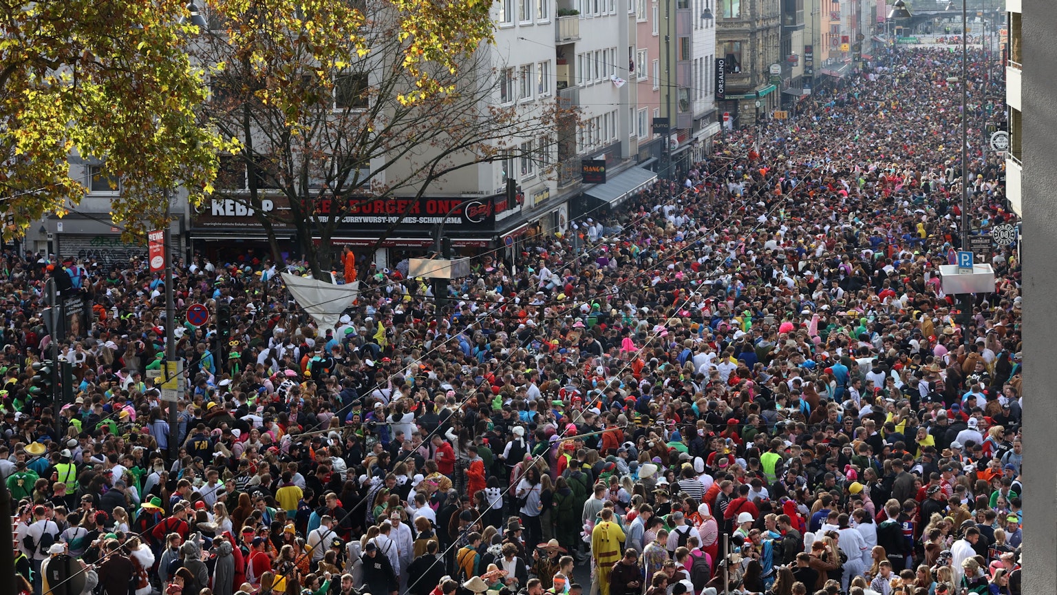 Blick aus einem Fenster auf die Zülpicher Straße, auf der sich Massen kostümierter Menschen drängen, die die gesamte Straßenbreite einnehmen.