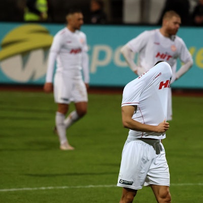 Drei Fußballspieler gehen vom Platz. Der vordere zieht sich enttäuscht das Trikot über den Kopf.