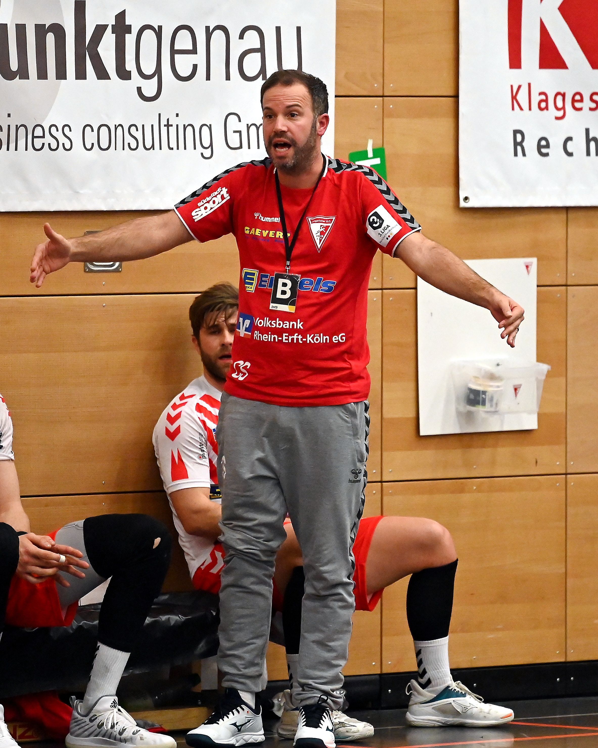 Ein Handballtrainer steht am Spielfeldrand und breitet die Arme aus.