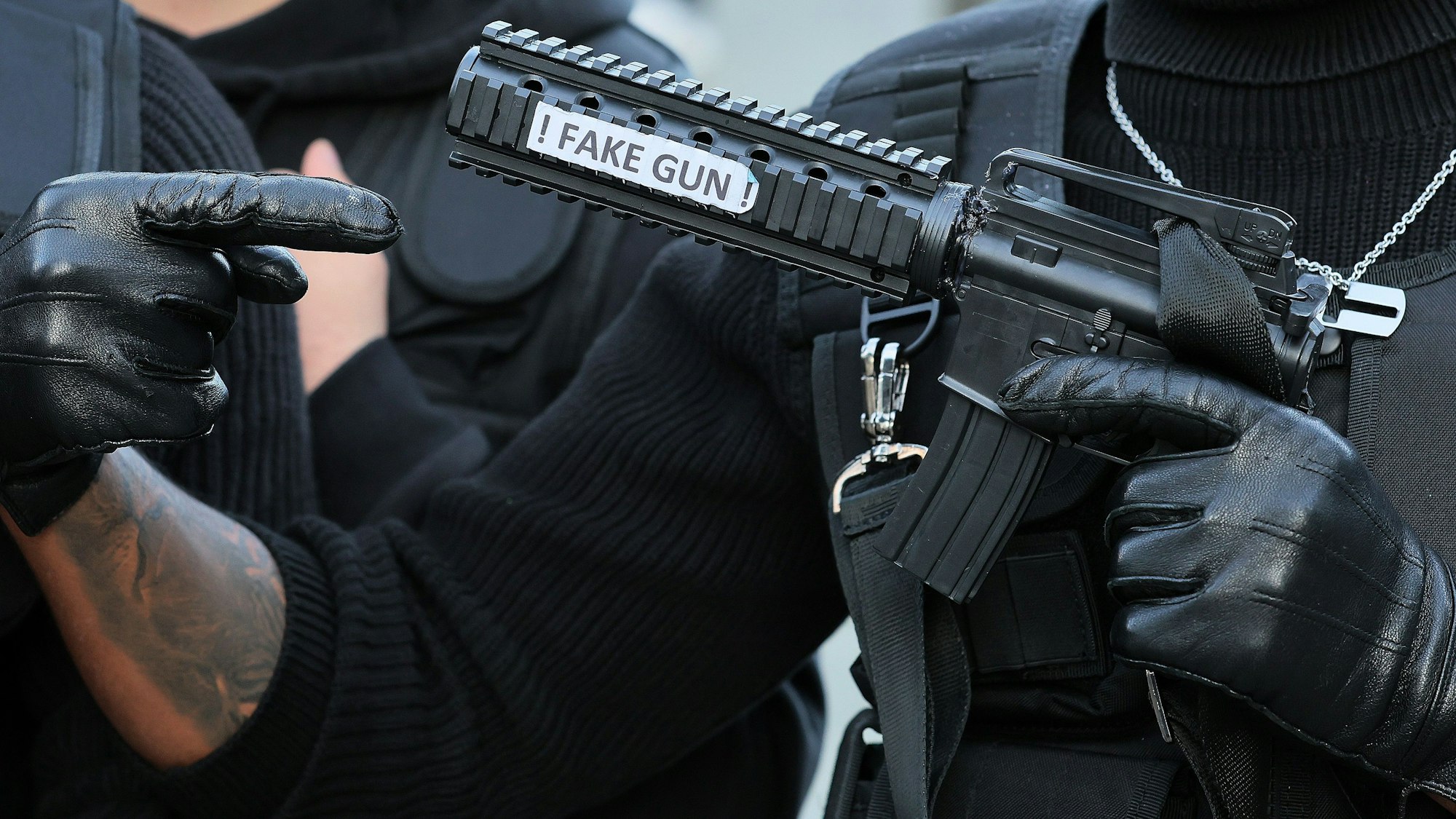 Ein als Swat-Polizist verkleideter Karnevalist hält eine Pistolenattrappe mit der Aufschrift „Fake Gun“ in der Hand.