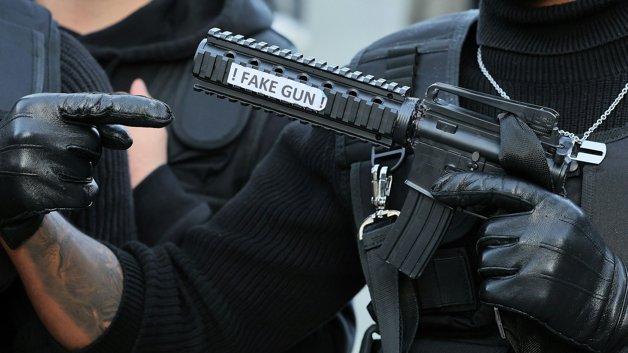 Ein Kostumierter trägt eine falsche Waffe mit der Aufschrift „fake gun“ vor sich.