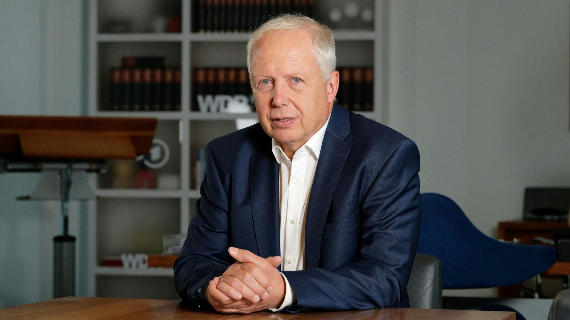 Tom Buhrow, Intendant des Westdeutschen Rundfunks, sitzt mit gefalteten Händen und offenem Hemdkragen in seinem Büro im Gebäude des WDR.