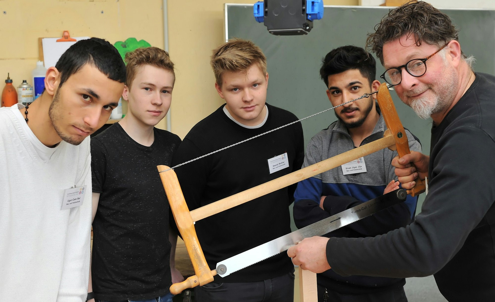 Ausbilder Arnulf Rückamp steht mit seinen Lehrlingen um einen Tisch mit Werkzeug und sägt Holz.