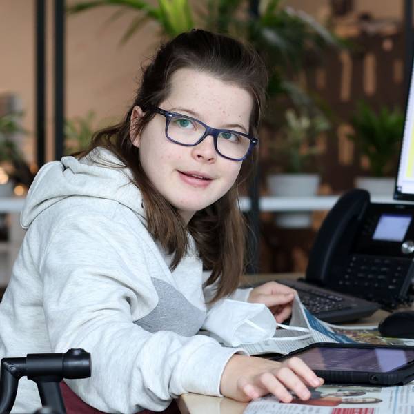 Die gehandicapte Schülerin Aimée Heimbach sitzt an einem Schreibtisch in der Lokalredaktion des Kölner Stadt-Anzeigers vor einem großen Monitor, auf dem die aktuelle Zeitungsseite zu sehen ist.