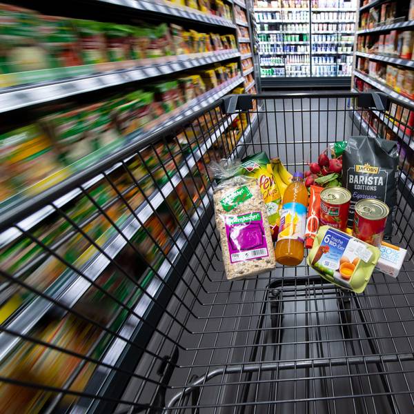 Ein Einkaufswagen, gefüllt mit Konserven, Eiern und einigen anderen Lebensmitteln, wird durch einen Gang im Supermarkt geschoben.