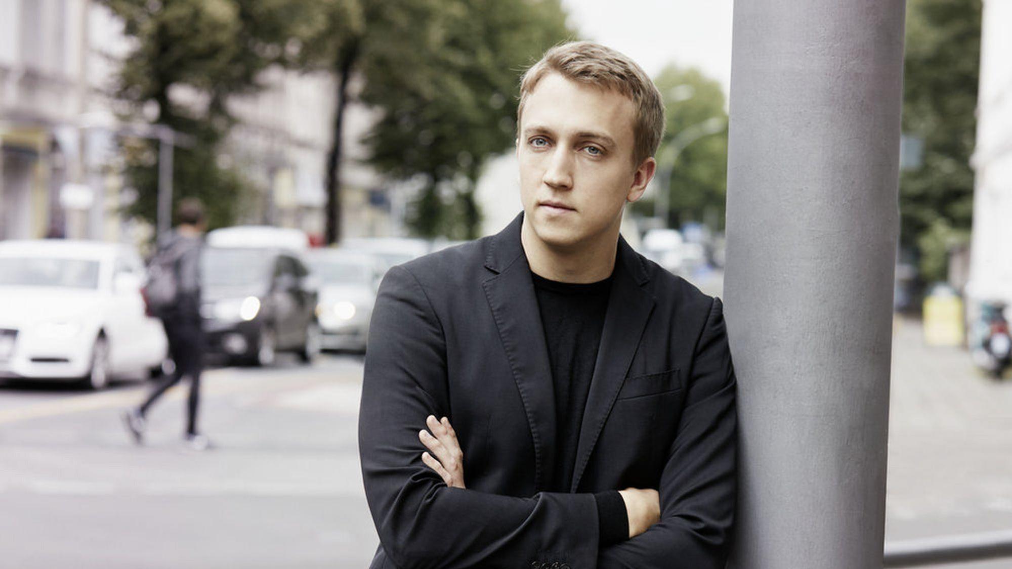 Der Kölner Pianist Fabian Müller, angelehnt an eine Straßenlaterne.