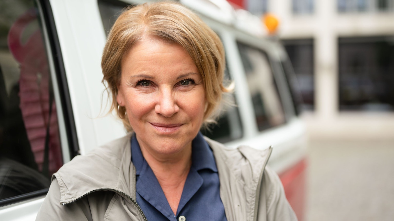 Die Schauspielerin Mariele Millowitsch steht neben einem Bulli und lächelt.