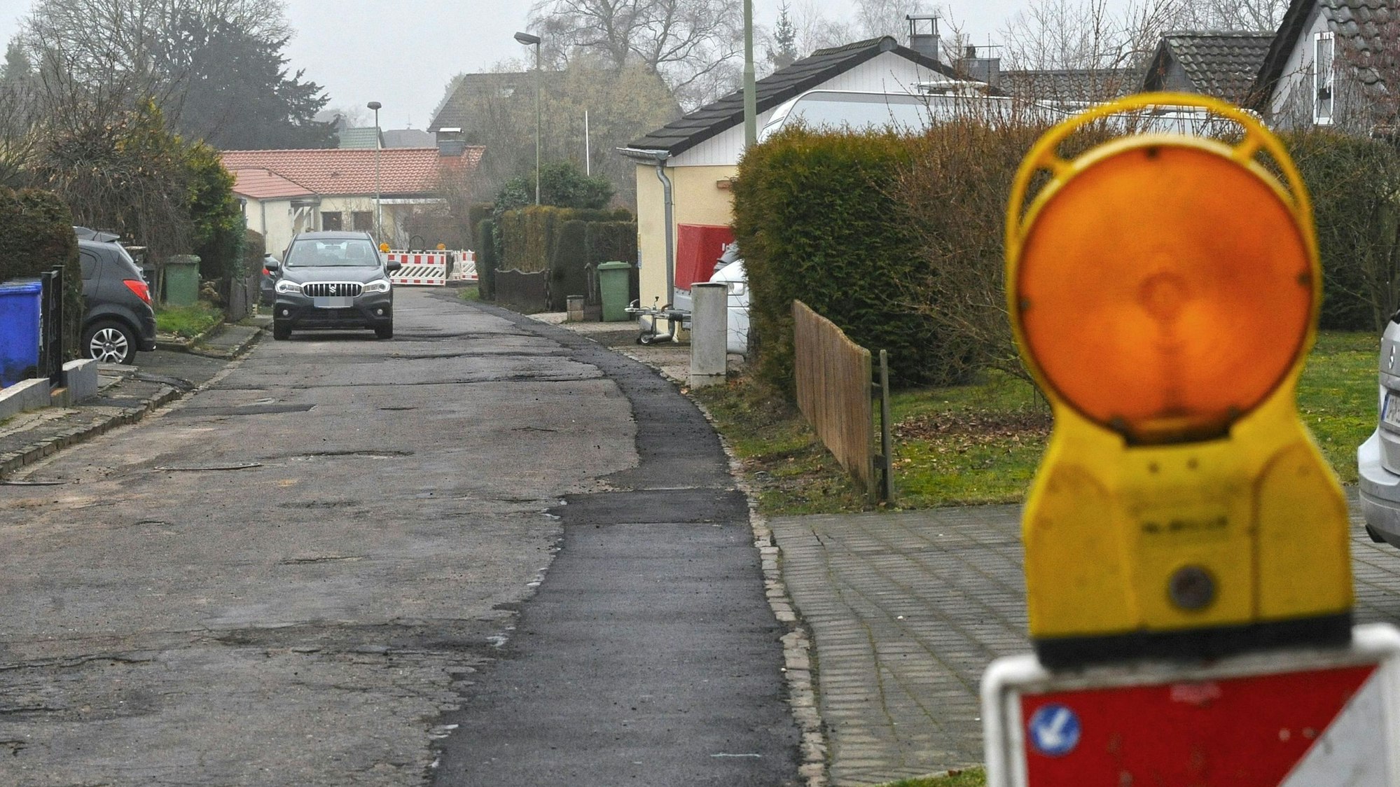 Die Straße Am Kreuzweg mit einer Warnleuchte im Vordergrund und parkenden Autos im Hintergrund.