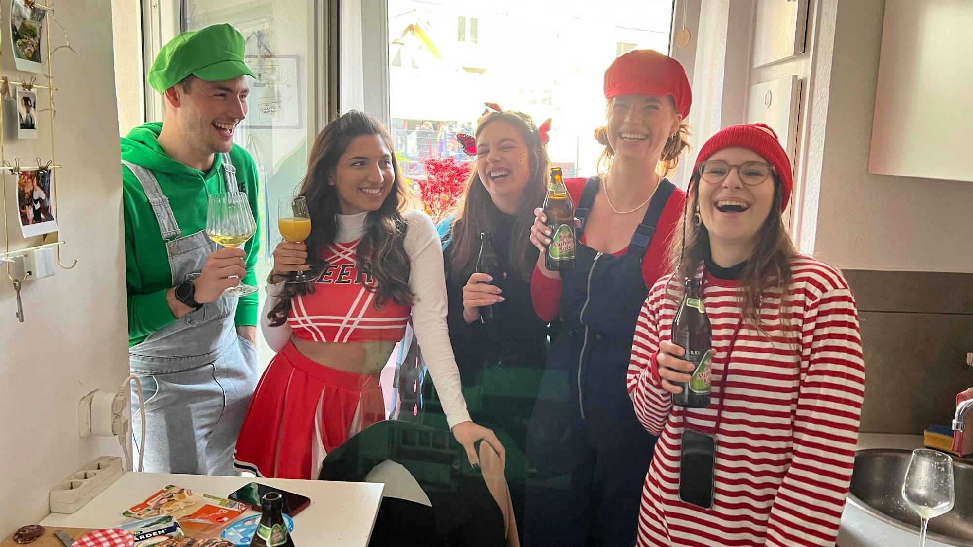 Eine Gruppe junger Menschen steht in einer Küche. Sie sind bunt kostümiert.