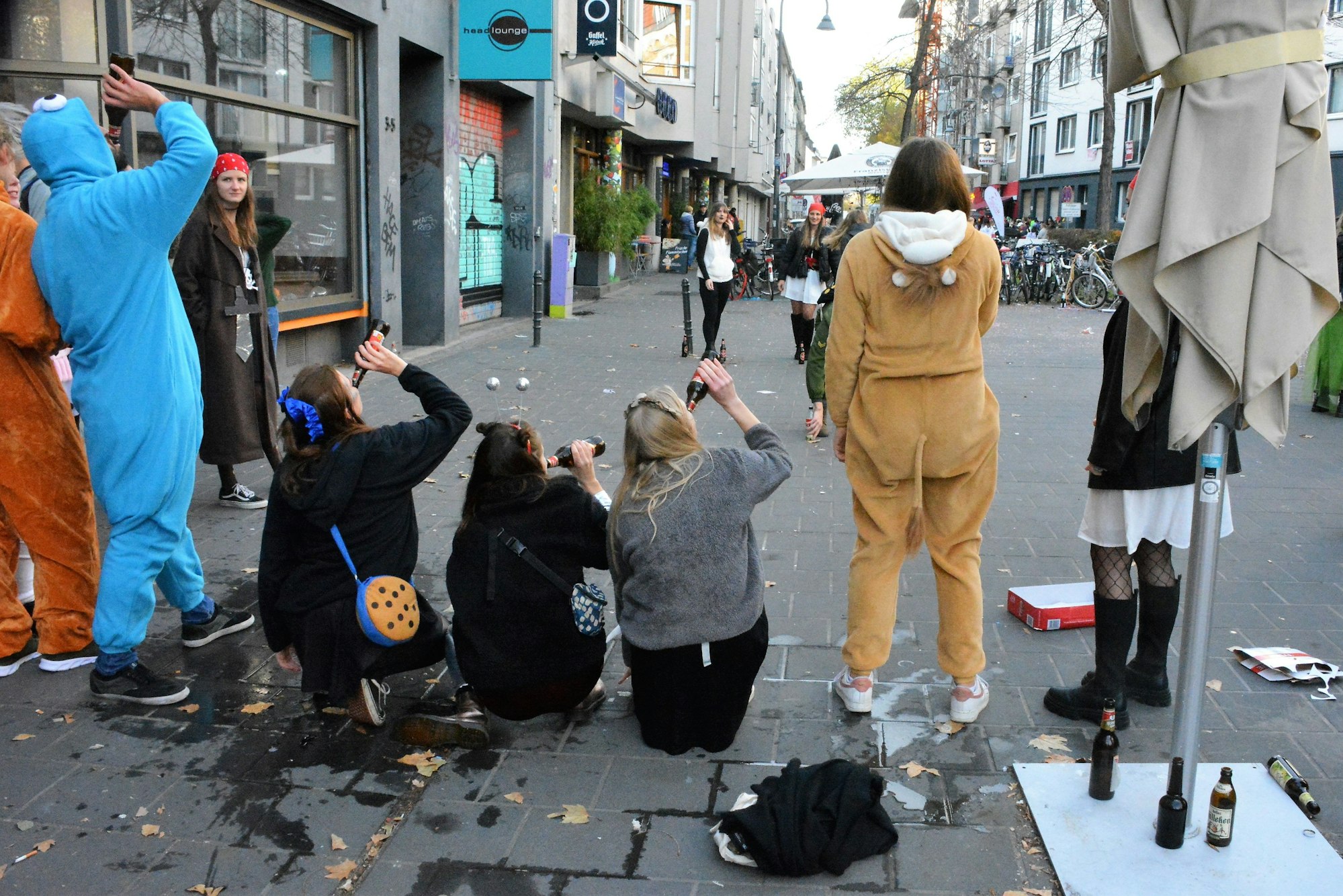 Mehrere Frauen hocken auf dem Bürgersteig und trinken aus Kölsch-Flachen bei der Bierball-Auseinandersetzung vor der Torburg.