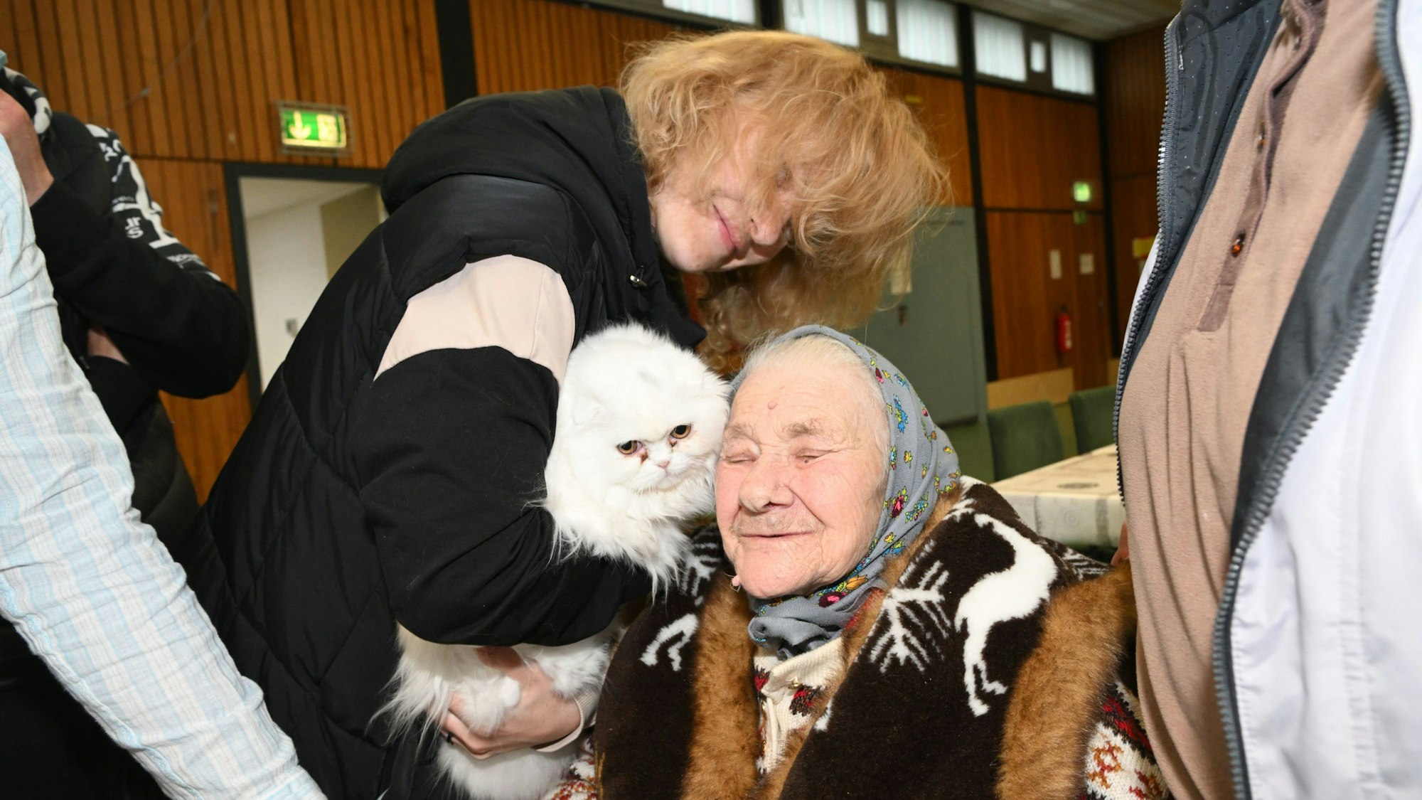 Eine Frau hält einer älteren Frau eine Katze entgegen. Sie sind in einer Notunterkunft.