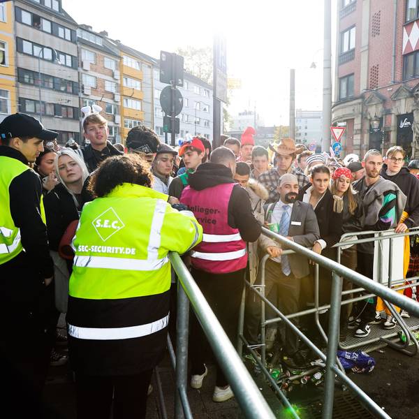 Junge kostümierte Menschen stehen am 11.11. vor Drängelgittern an einer Absperrung auf der Luxemburger Straße