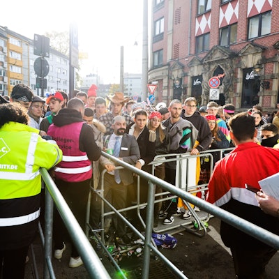 Kostümierte Menschen stehen am 11.11.2022 am Eingang zur Party-Zone auf der Zülpicher Straße vor einer Absperrung.