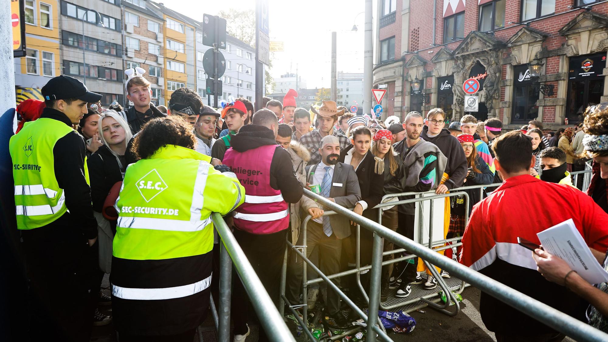 Kostümierte Menschen stehen am 11.11.2022 am Eingang zur Party-Zone auf der Zülpicher Straße vor einer Absperrung.