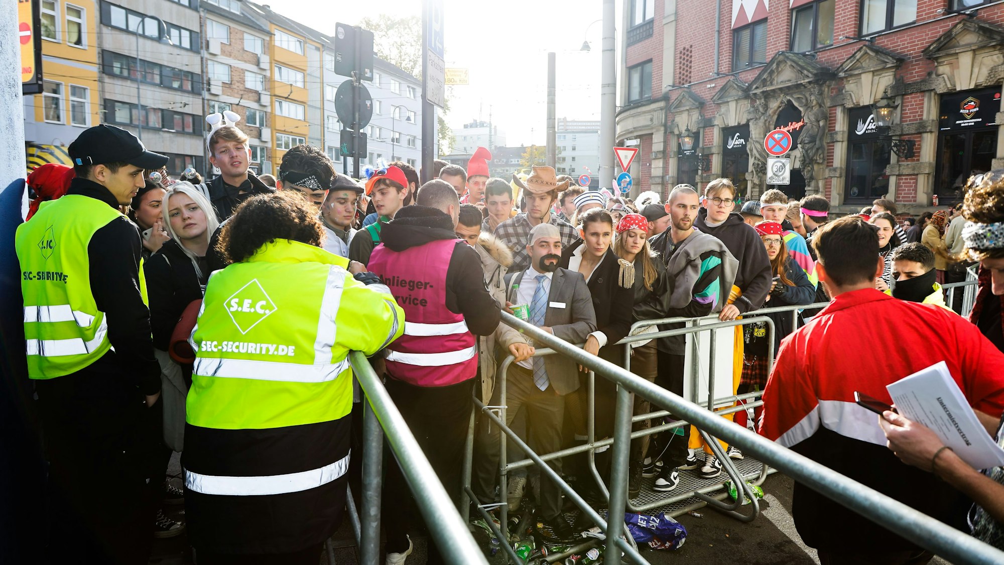 Kostümierte Menschen stehen am 11.11.2022 am Eingang zur Party-Zone auf der Zülpicher Straße vor einer Absperrung.