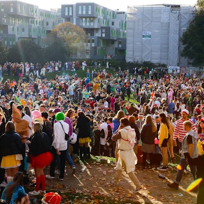 Hunderte Karnevalisten stehen am 11.11. auf einer Wiese vor der Universität.