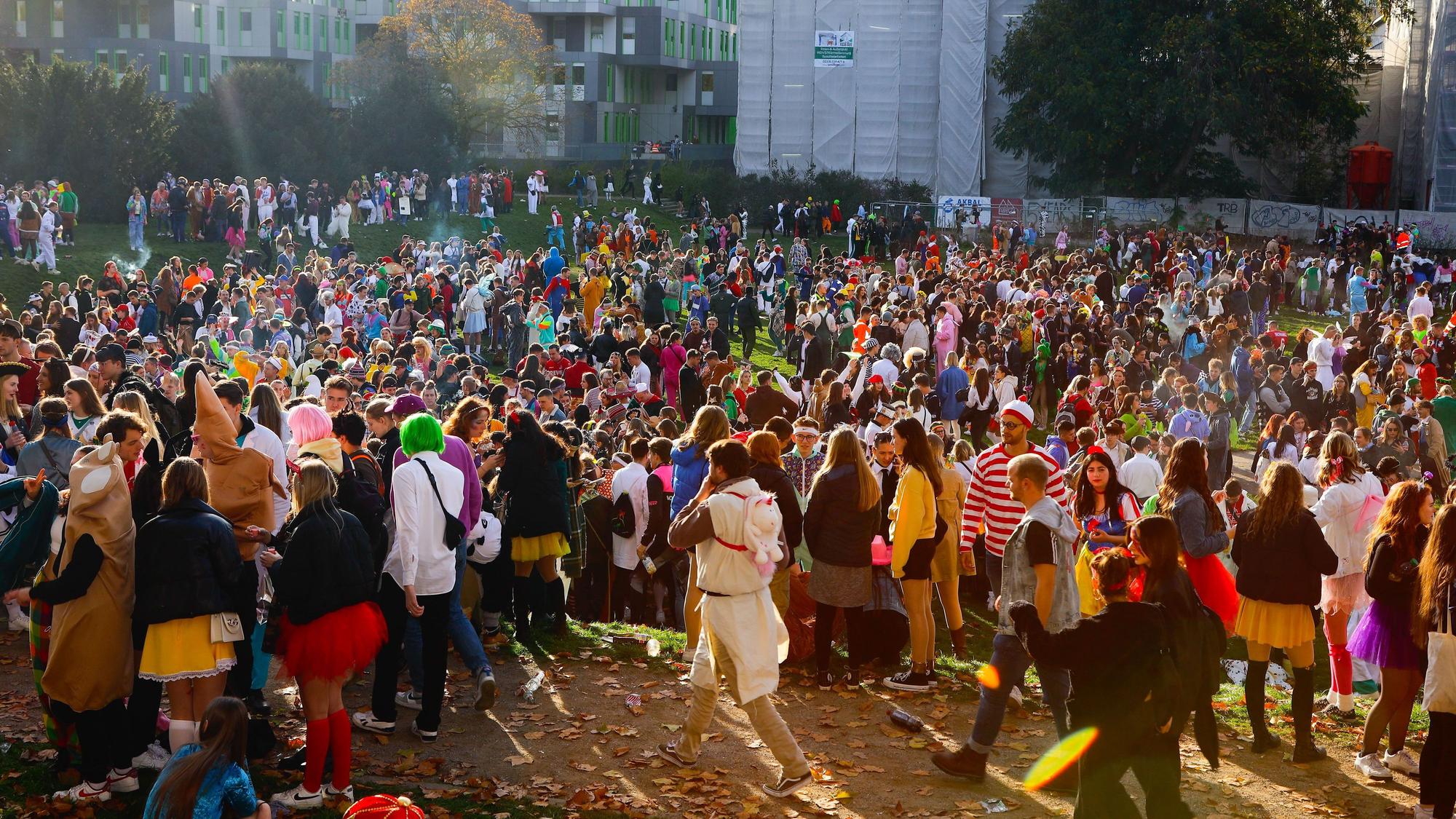 Hunderte Karnevalisten stehen am 11.11. auf einer Wiese vor der Universität.