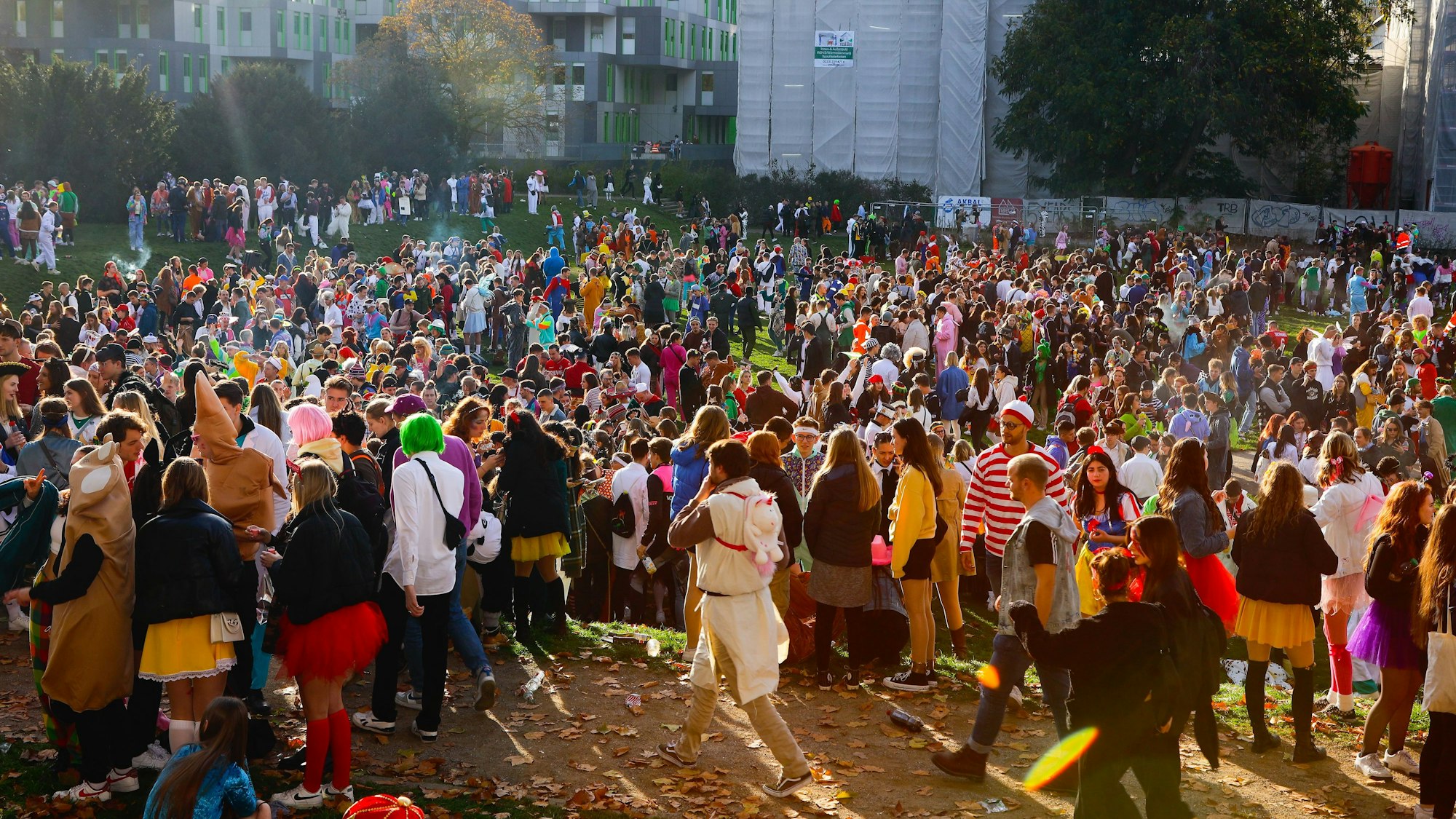 Hunderte Karnevalisten stehen am 11.11. auf einer Wiese vor der Universität.