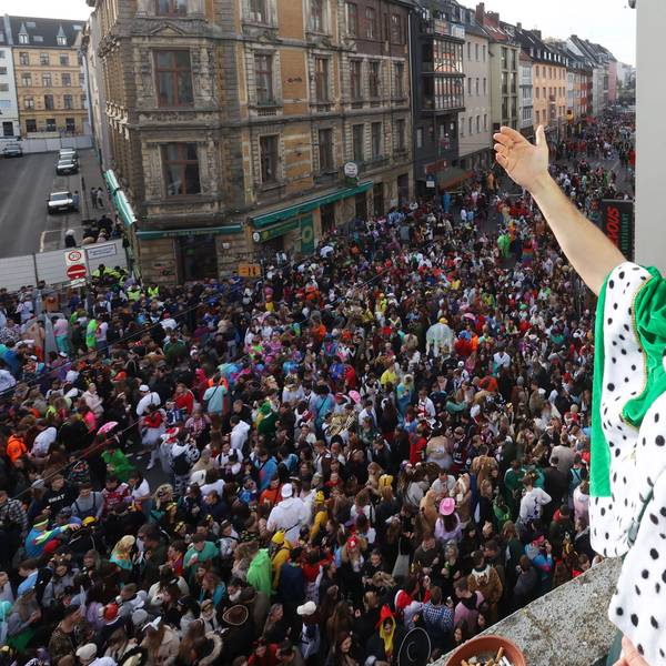 Ein junger Mann steht mit einer Krone auf dem Balkon. Unter ihm die volle Zülpicher Straße.