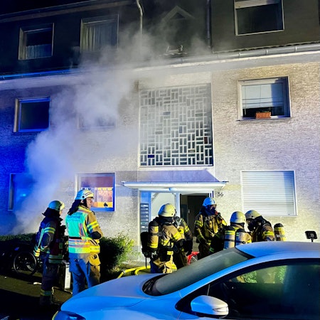 Aus einem Haus steigt Qualm auf. Vor dem Haus stehen mehrere Feuerwehrleute.