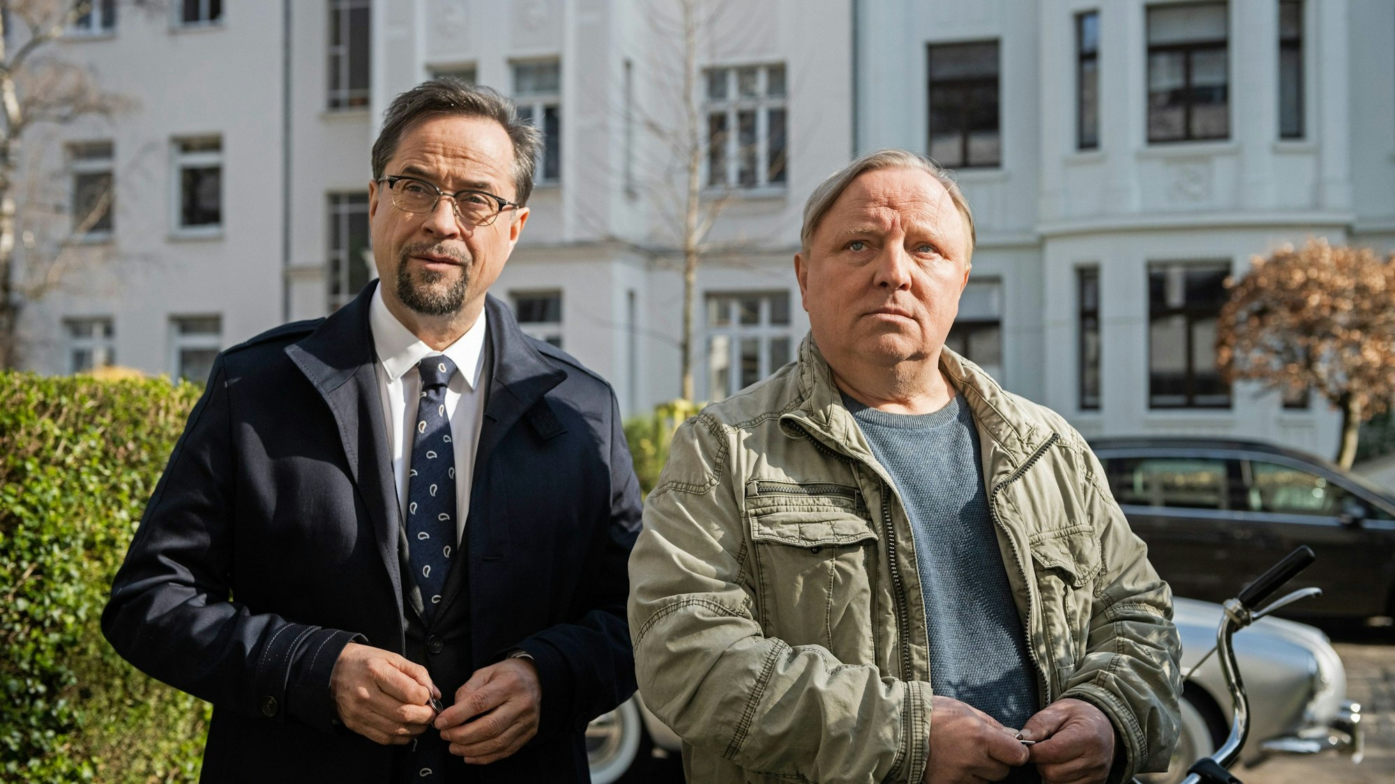 Der Rechtsmediziner Prof. Karl-Friedrichs Boerne (Jan Josef Liefers, l) und Kommissar Frank Thiel (Axel Prahl) in einer Außenaufnahme in Münster, im Hintergrund Häuser und eine Hecke.
