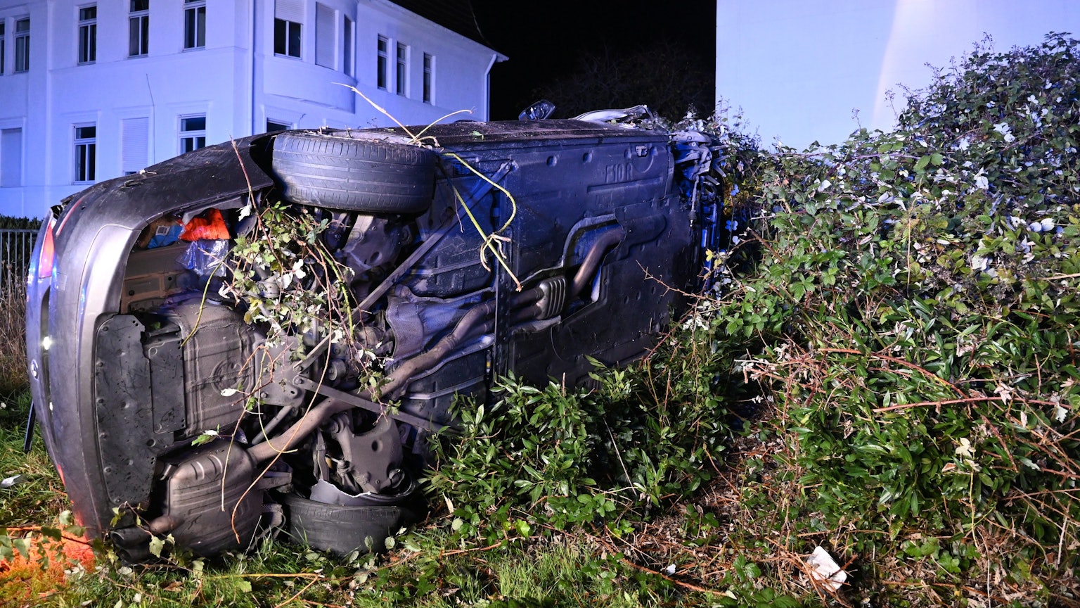 Ein Auto liegt auf der Seite in einem Gebüsch neben der Straße.