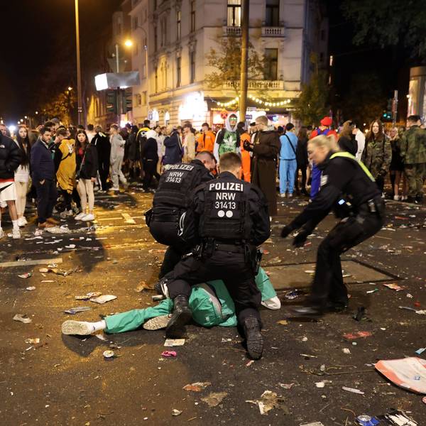 Polizisten beugen sich über einen Karnevalisten in grünem Kostüm. Rundherum stehen Menschentrauben.