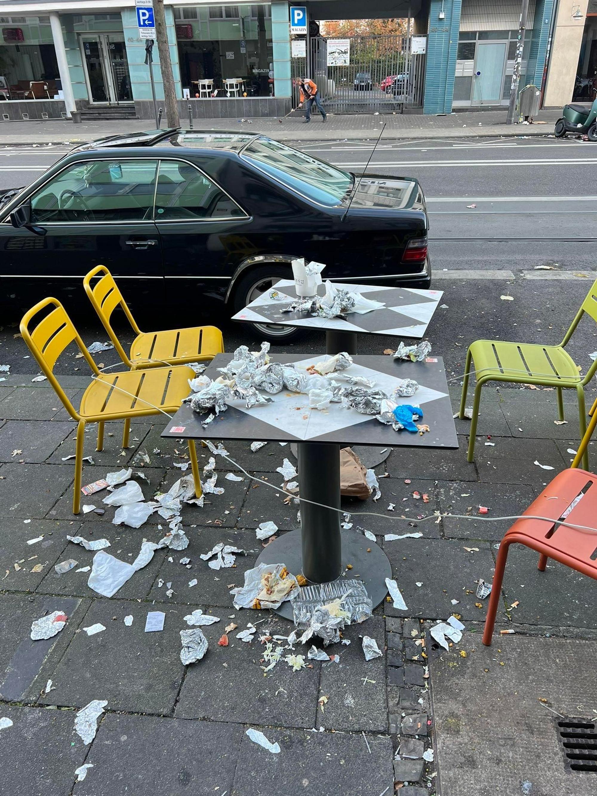 Ein Tisch mit vier Stühlen vor einer Gaststätte an der Aachener Straße ist mit Müll übersät.