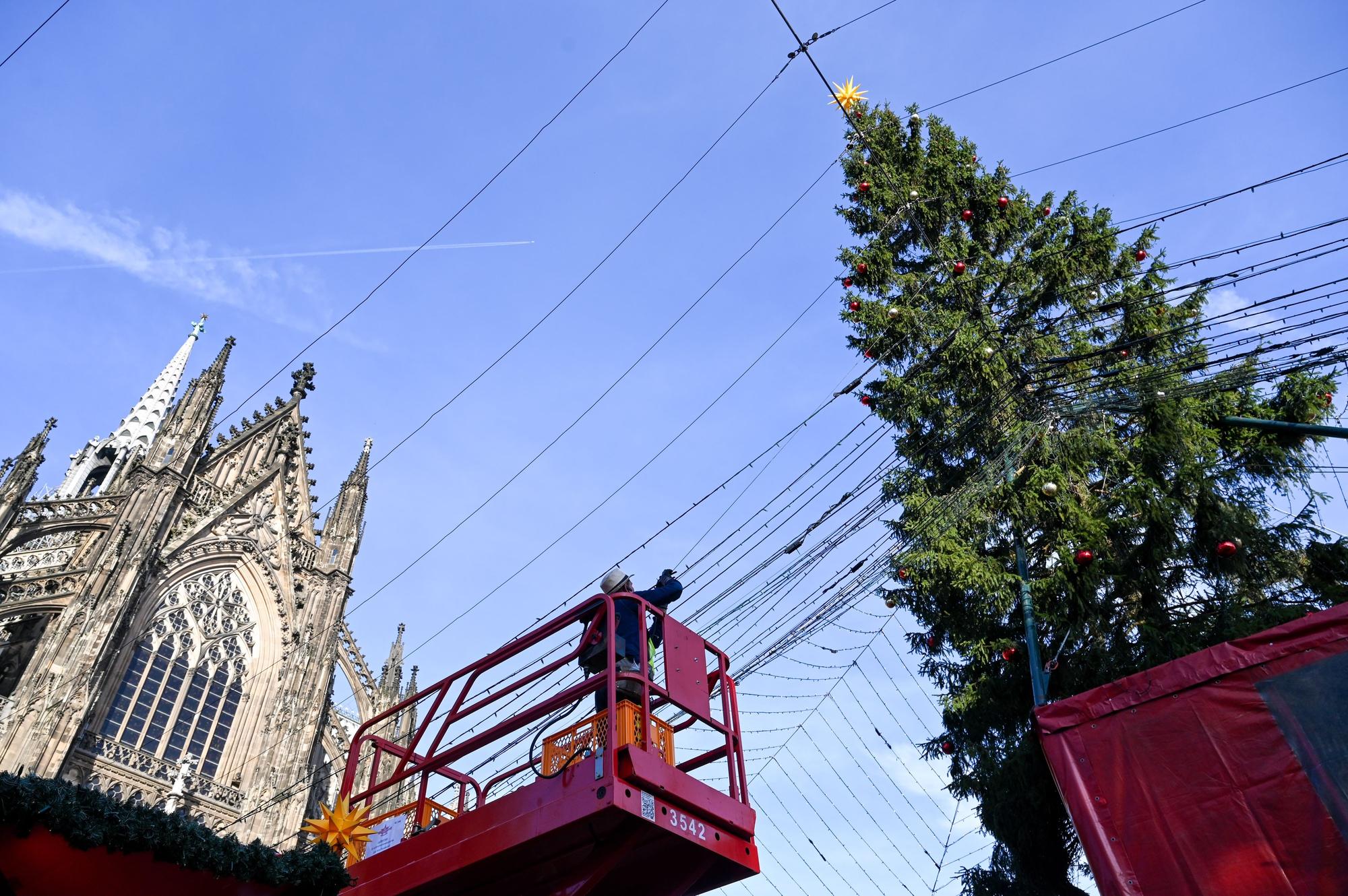 Ein Arbeiter steht auf einer Hebebühne und installiert Lichterketten, die sich über den Weihnachtsmarkt am Roncalliplatz spannen werden.