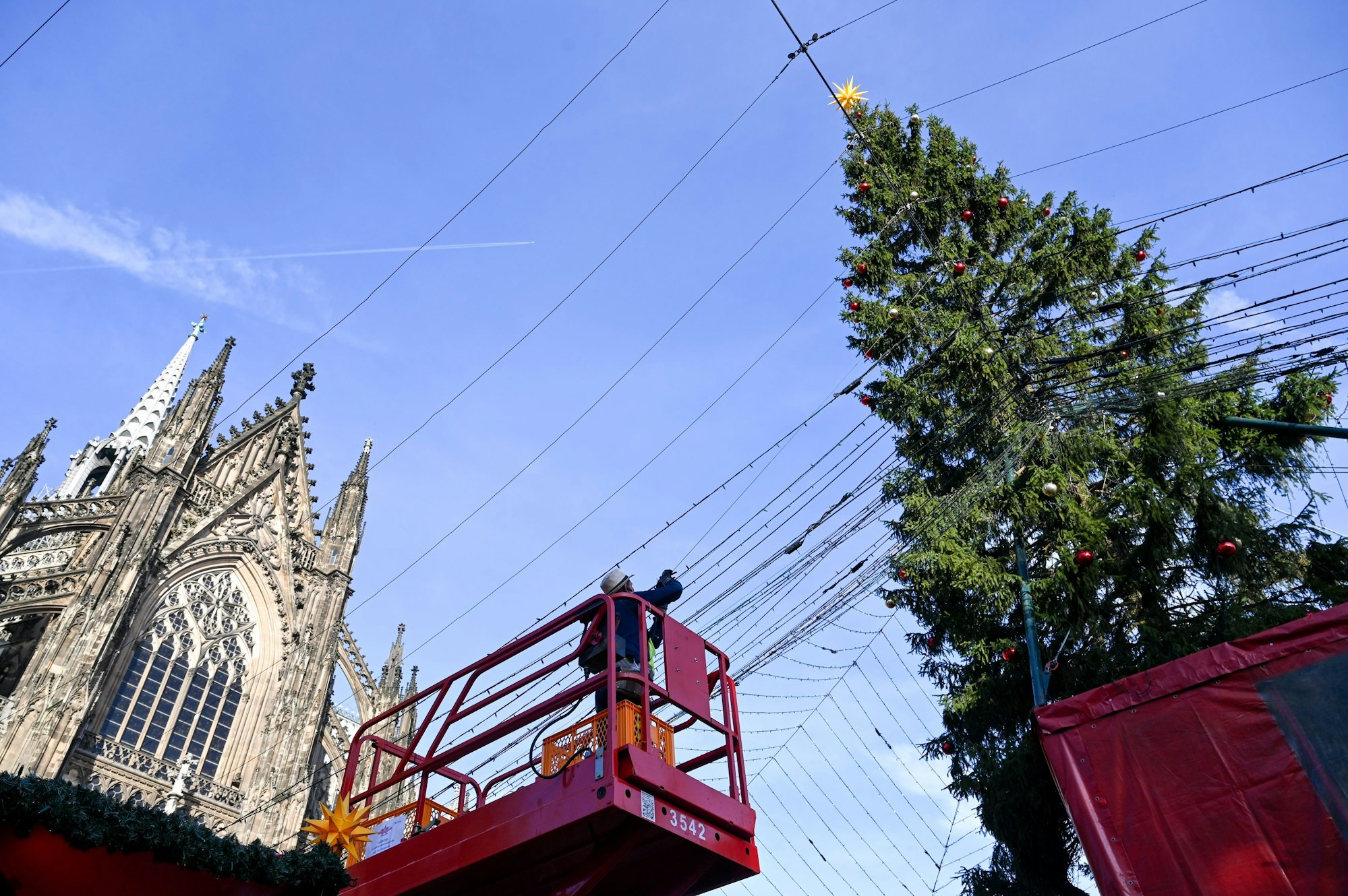 Ein Arbeiter steht auf einer Hebebühne und installiert Lichterketten, die sich über den Weihnachtsmarkt am Roncalliplatz spannen werden.
