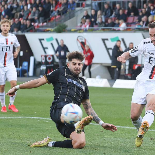 Ein Fußballspieler flankt den Ball vors Tor und sein Gegenspieler versucht es zu verhindern.