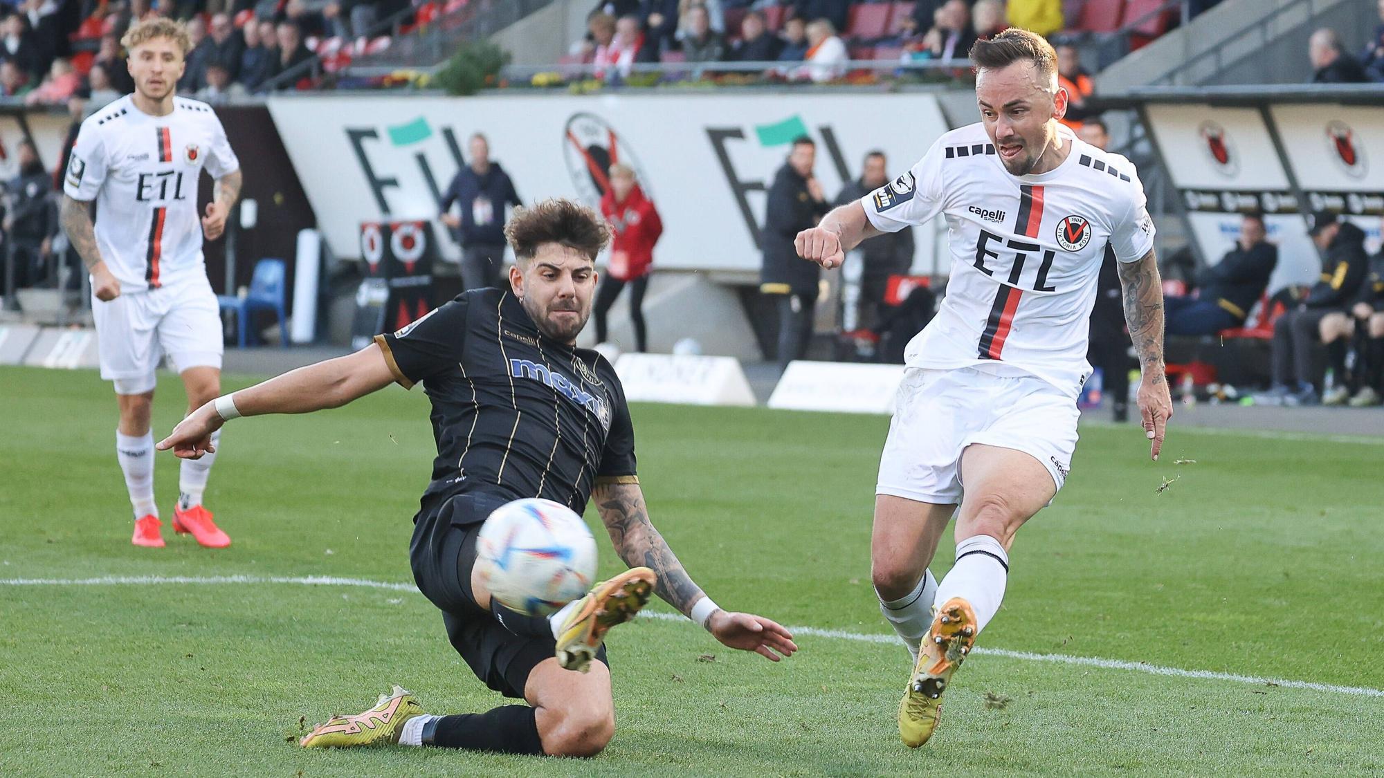 Ein Fußballspieler flankt den Ball vors Tor und sein Gegenspieler versucht es zu verhindern.