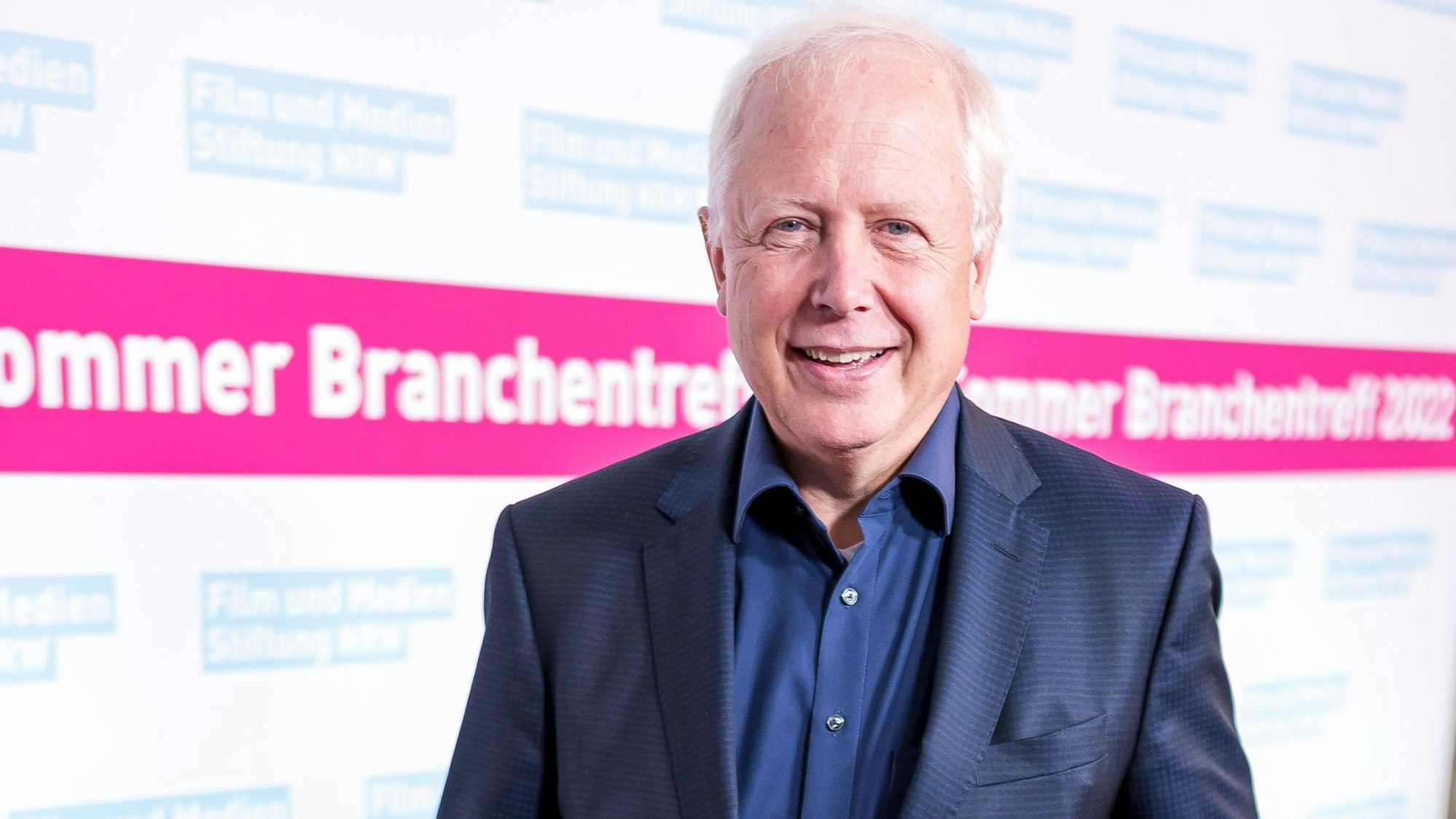 WDR-Intendant Tom Buhrow. vor einer Plakatwand mit der Aufschrift „Sommer Branchentreff 2022“.