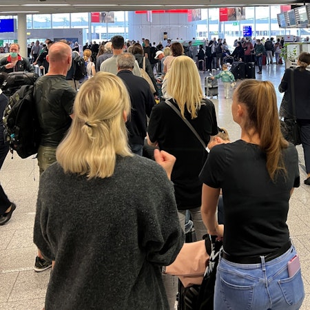 Ferienfluggäste stehen in einer langen Schlange am Frankfurter Flughafen.