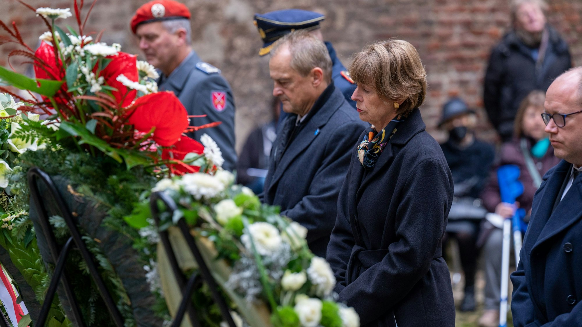 Henriette Reker steht mit anderen Teilnehmern mit gefalteten Händen vor einem Trauerkranz.