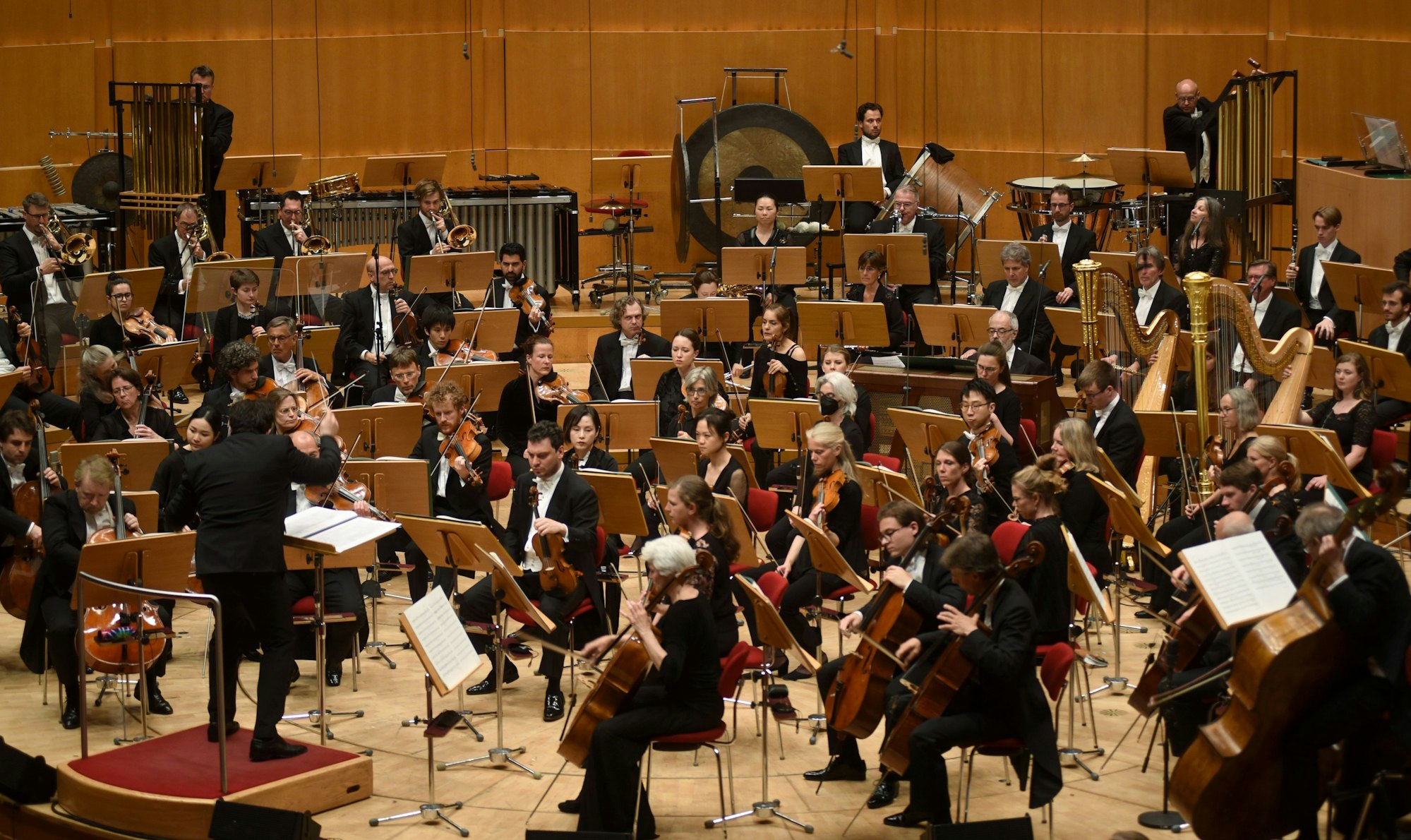 Chef-Dirigent Cristian Macelaru steht mit dem Rücken zur Kamera und dirigiert das WDR-Sinfonieorchester in einem Konzertsaal.